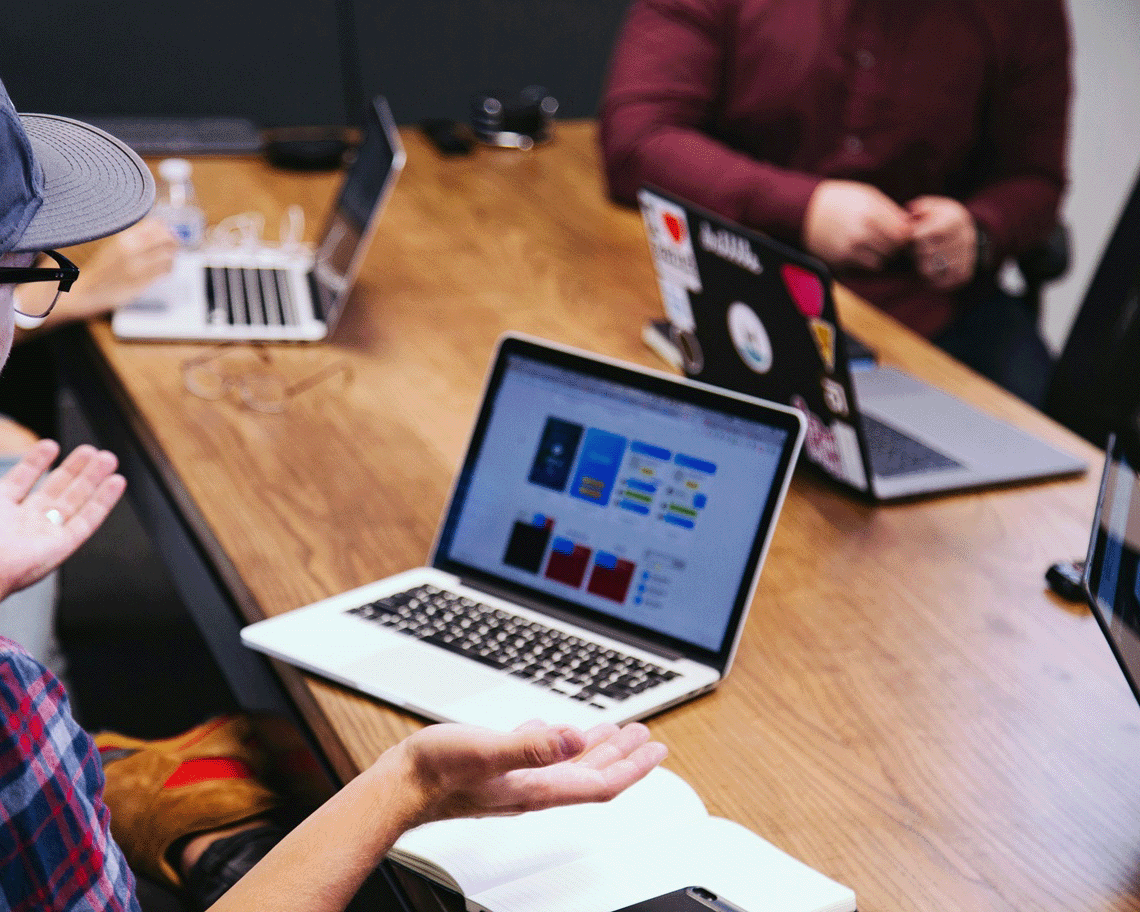 Laptops sit on the desk within an office environment. A team of experts lead a conversation.